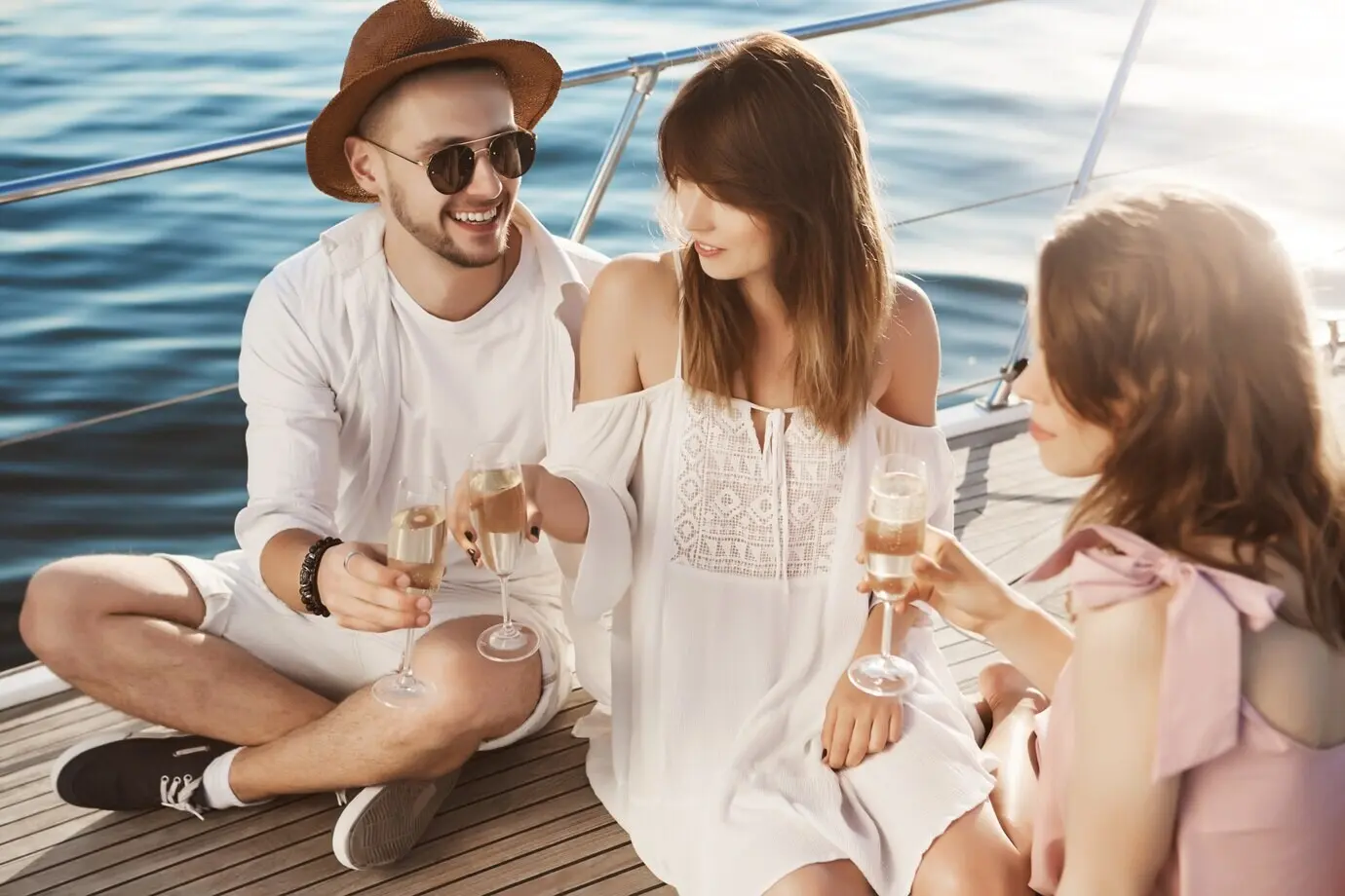 Porträt eines Paares und einer befreundeten Person, die auf einer Yacht sitzen, trinken und fröhlich Zeit miteinander verbringen. Eine erwachsene Person nippt in trendiger Kleidung im Luxusurlaub an Champagner.